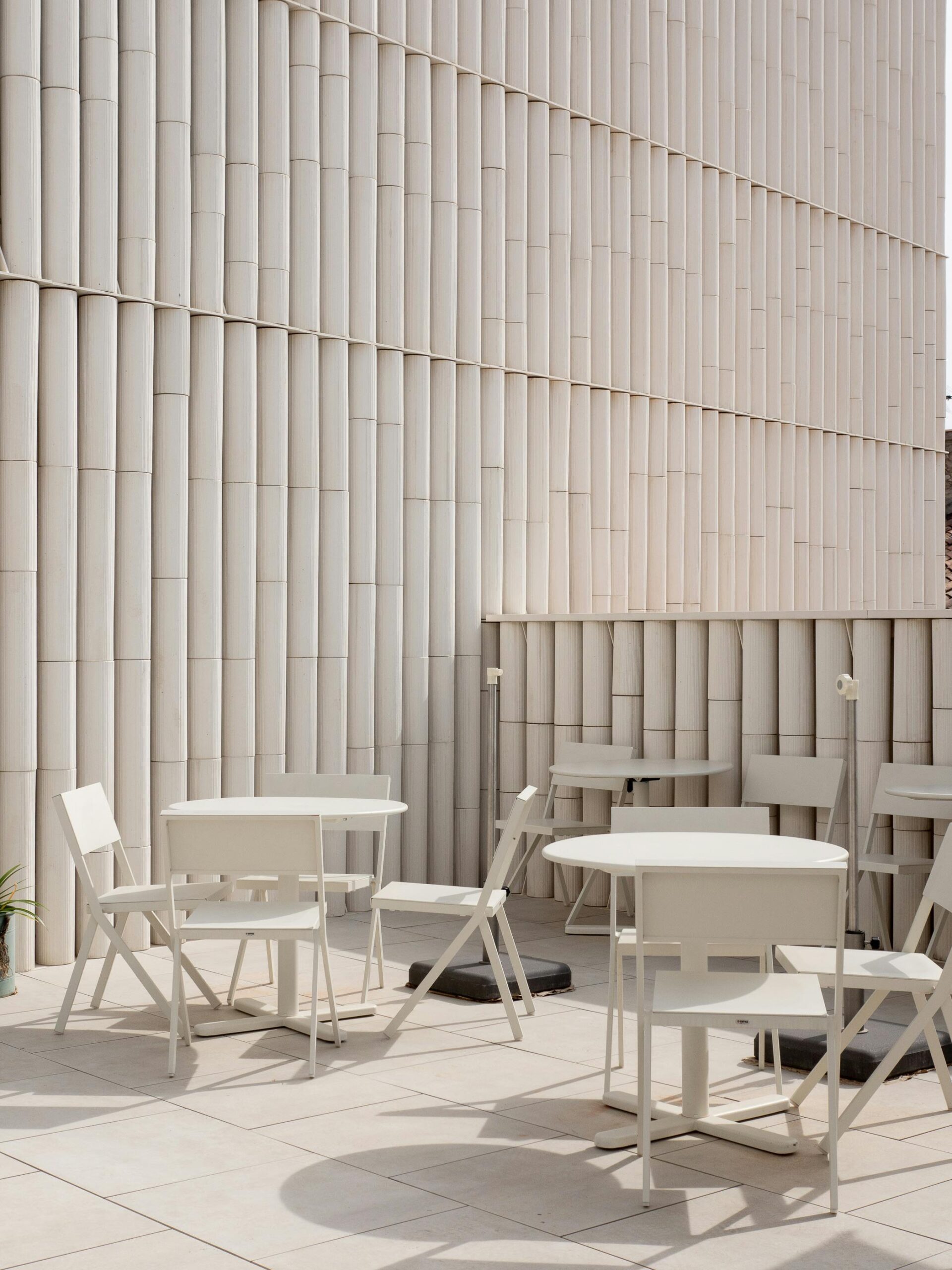 Elegant outdoor patio scene with white chairs and tables against a textured wall.