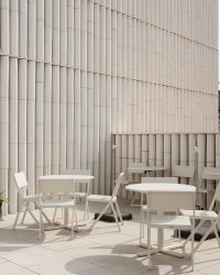 pexels-photo-21048245-21048245 Elegant outdoor patio scene with white chairs and tables against a textured wall.
